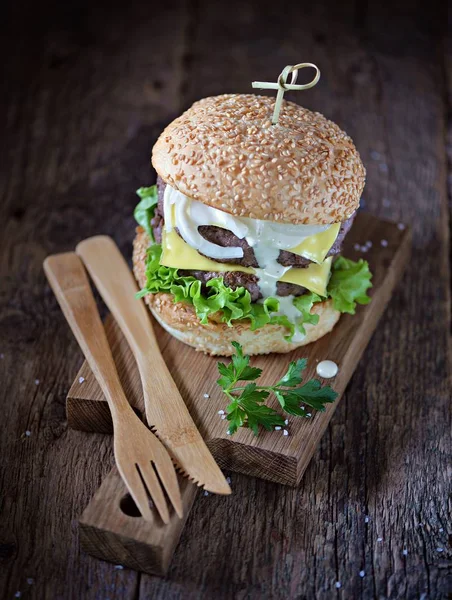 Σπιτικό, διπλό cheeseburger με μαρινάτο κρεμμύδι και σάλτσα λευκού σε μια μερίδα σκάφους σε ένα παλιό ξύλινο φόντο. — Φωτογραφία Αρχείου