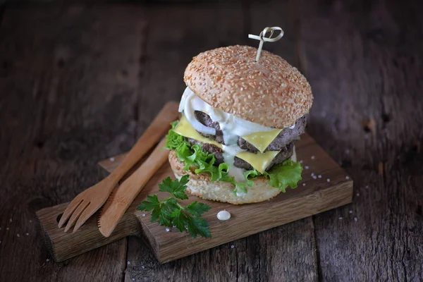 W domu dwukrotnie cheeseburger z cebulą marynowane i białym sosie na pokładzie służąc na stare podłoże drewniane. — Zdjęcie stockowe