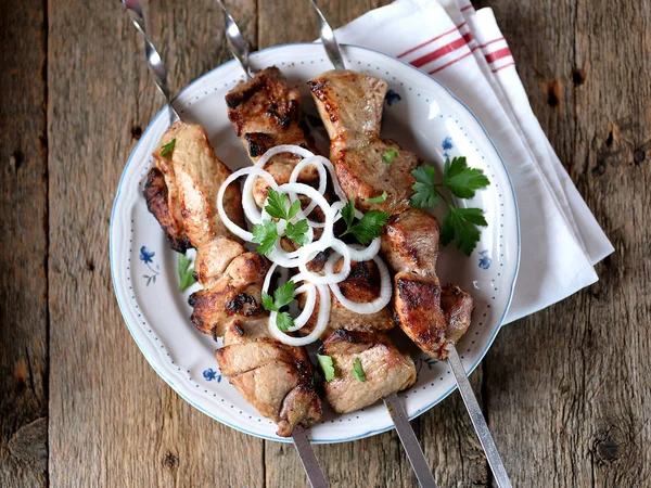 Huis shish kebab van varkensvlees op spiesjes met ingemaakte UI en peterselie op een oude houten achtergrond. — Stockfoto