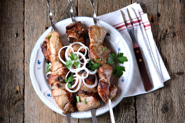 Huis shish kebab van varkensvlees op spiesjes met ingemaakte UI en peterselie op een oude houten achtergrond. — Stockfoto