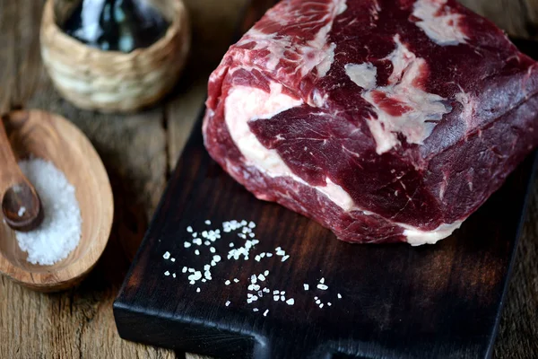 Steak de bœuf cru frais avec sel de mer sur une planche de service sur un vieux fond en bois . — Photo