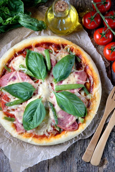 Házi pizza sonka, paradicsom, zöld bab, sajt és bazsalikom. Rusztikus stílusban. — Stock Fotó