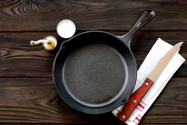 Cast-iron frying pan with salt and pepper on a wooden background. — Stock Photo, Image