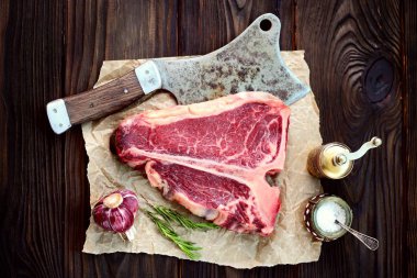Sarımsak ve biberiye eski bir ahşap zemin üzerinde ham t-bone biftek. Rustik tarzı.