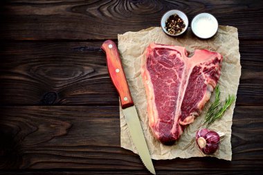 Sarımsak ve biberiye eski bir ahşap zemin üzerinde ham t-bone biftek. Rustik tarzı.