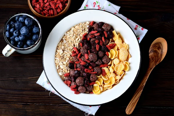 Petit déjeuner sain composé de flocons de maïs, boules de chocolat, flocons d'avoine, baies de goji et bleuets frais . — Photo