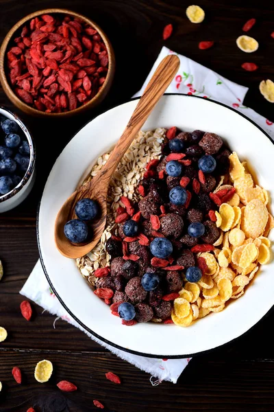 Healthy breakfast of cornflakes, chocolate balls, oatmeal, goji berries and fresh blueberries. — Stock Photo, Image