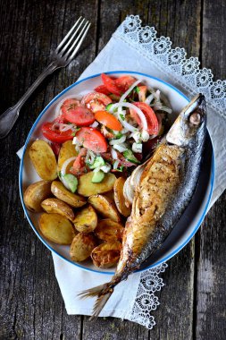 Uskumru bebek patates, biberiye, dereotu ve maydanoz, tatlı soğan ve baharatlar ile pişmiş. Taze sebze - domates, salatalık, tatlı soğan, dereotu, maydanoz ve zeytinyağı bir salata ile servis.