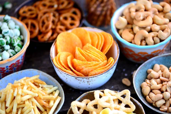 Different kinds of snacks - chips, salted peanuts, cashews, peas with wasabi, pretzels with salt, potatoes, salted straw. — Stock Photo, Image