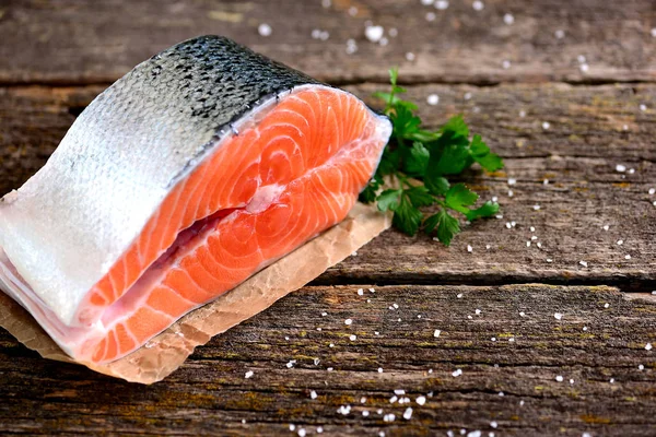 Stück frischer roher Lachs mit Bio-Petersilie auf altem Holzgrund. — Stockfoto