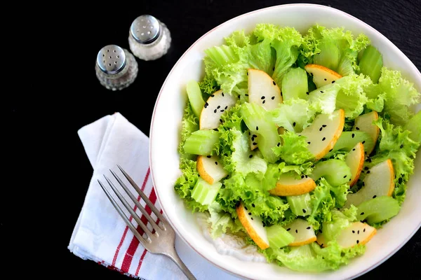 Healthy salad from organic pear, celery sticks, lettuce, olive oil, balsamic vinegar and sesame. — Stock Photo, Image