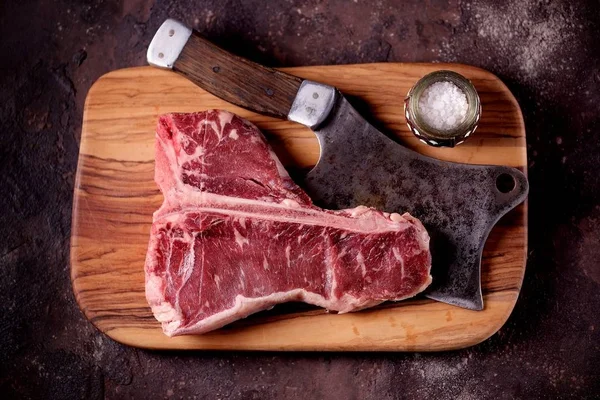 Taze çiğ t-bones biftek bir zeytin ahşap tahta deniz tuzu ile ve bir mutfak balta. Üstten Görünüm.