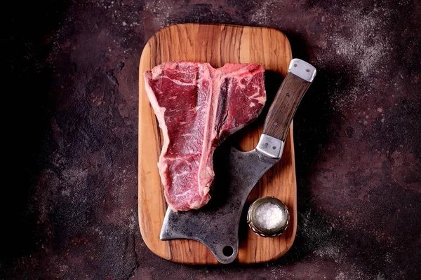 Taze çiğ t-bones biftek bir zeytin ahşap tahta deniz tuzu ile ve bir mutfak balta. Üstten Görünüm.