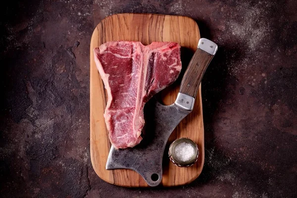 Taze çiğ t-bones biftek bir zeytin ahşap tahta deniz tuzu ile ve bir mutfak balta. Üstten Görünüm.