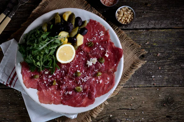 Beef Carpaccio Parmesan Arugula Pickled Cucumbers Squash Dried Olives Capers — Stock Photo, Image