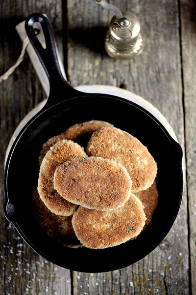 Fish cutlets in breadcrumbs in a cast-iron frying pan.