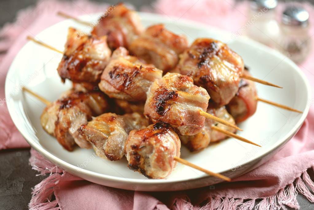 Shish kebab from pork in bacon on wooden skewers roasted on a cast-iron frying pan.