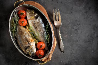İki taze kekik, cherry domates, kırmızı soğan ve limon bakır tavada balık dorado pişmiş.