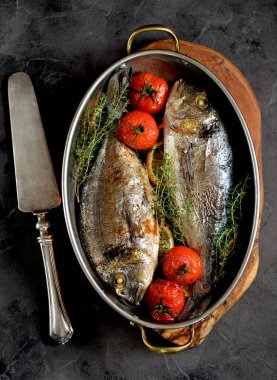 İki taze kekik, cherry domates, kırmızı soğan ve limon bakır tavada balık dorado pişmiş.