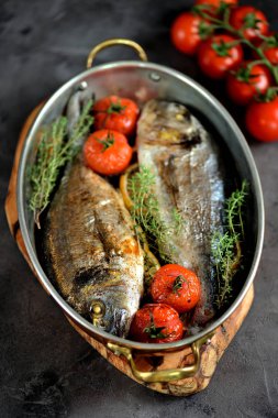 İki taze kekik, cherry domates, kırmızı soğan ve limon bakır tavada balık dorado pişmiş.