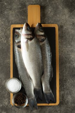 Gri arka planda servis panosunda üç taze çiğ levrek. Üst görünüm. 