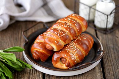 Hamur mayasında ev yapımı sosisler, tahtadan bir arka planda susam tohumu ve süt..