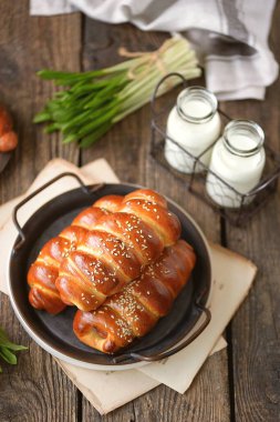 Hamur mayasında ev yapımı sosisler, tahtadan bir arka planda susam tohumu ve süt..