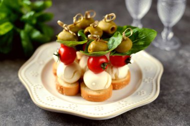 Mozzarella kanepeleri, yeşil zeytin, kiraz domatesleri, kızarmış ekmek üzerine fesleğen..