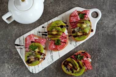 Yumuşak peynirli sandviç, kivi, kurutulmuş sosis ve balzamik krema..