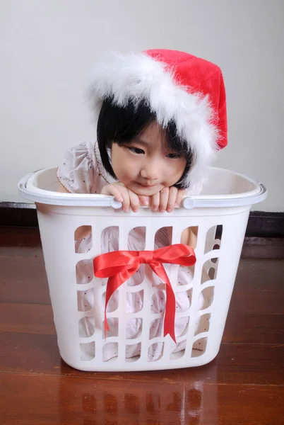 Мила азіатська маленька дівчинка в капелюсі Санта сидить у подарунковому кошику — стокове фото