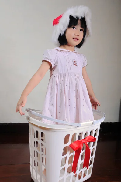 Lindo asiático niña en un santa sombrero de pie en regalo cesta —  Fotos de Stock