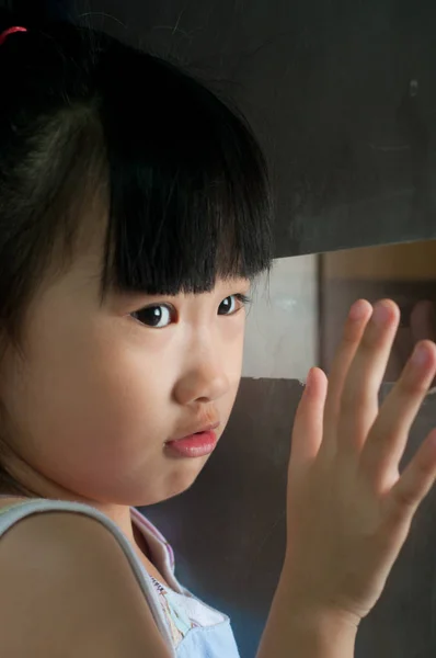 Sad asian child waits for someone near the window