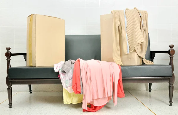 Cajas de cartón y pila de ropa en un sofá negro — Foto de Stock