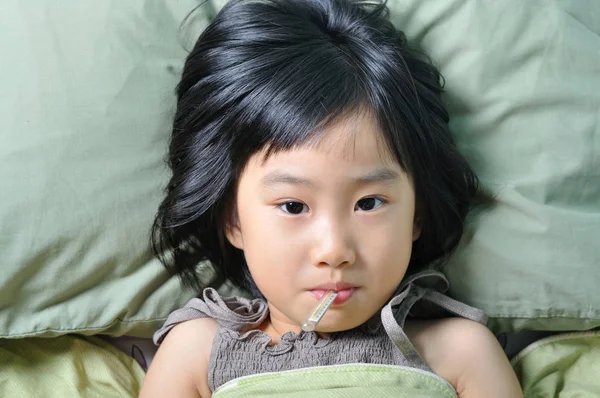 Маленька азіатська хвора дівчинка під ковдрою з температурою в роті — стокове фото