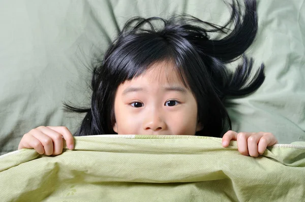 Scared little asian girl hiding behind blanket