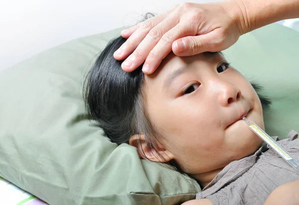 Маленькая больная девочка с температурой во рту и заботливой мотылькой — стоковое фото