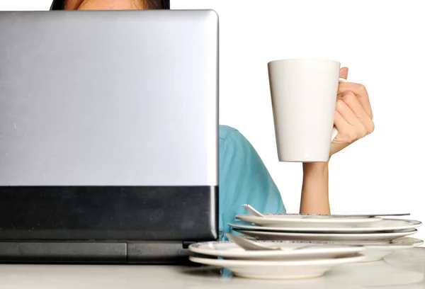 hand holding a cup behind laptop and stack of dirty plates on wo