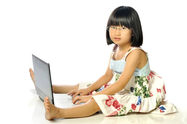 Kleines Mädchen mit Brille, das mit einem Laptop auf dem Boden sitzt, weiß — Stockfoto