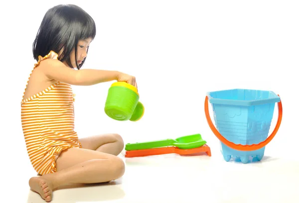 Азиатская маленькая девочка в купальнике играет с пляжными игрушками на белом — стоковое фото