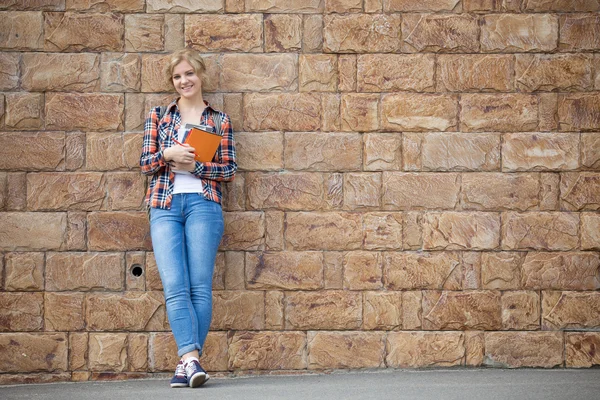 Full längd porträtt av student flicka mot tegelväggen med läroböcker — Stockfoto