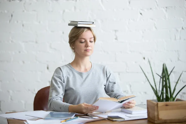 Porträtt av attraktiv kvinna vid skrivbord, böcker på hennes huvud — Stockfoto