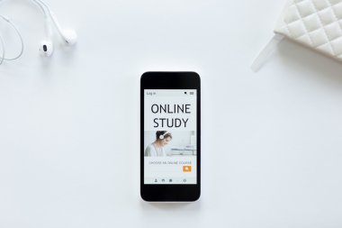 White office desk with earphones, mobile phone, online study on screen