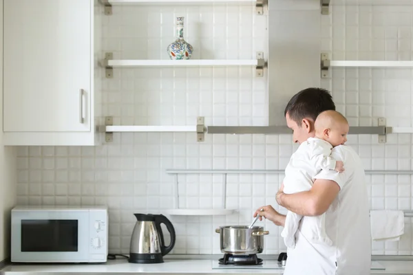 Man in the kitchen holding a child on shoulder, cooking — Stock Photo, Image