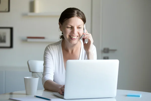 Porträtt av leende kvinna nära laptop pratar i telefon. — Stockfoto