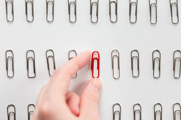Hand picking among metal paperclips one red, different from others — Stock fotografie