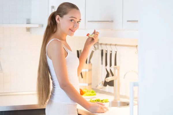 Portrait of a young woman tasting a green salad on the kitchen, — Stock Photo, Image