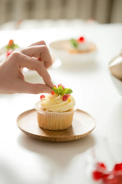 Nahaufnahme einer weiblichen Hand, die einen Cupcake mit Minzblatt dekoriert — Stockfoto