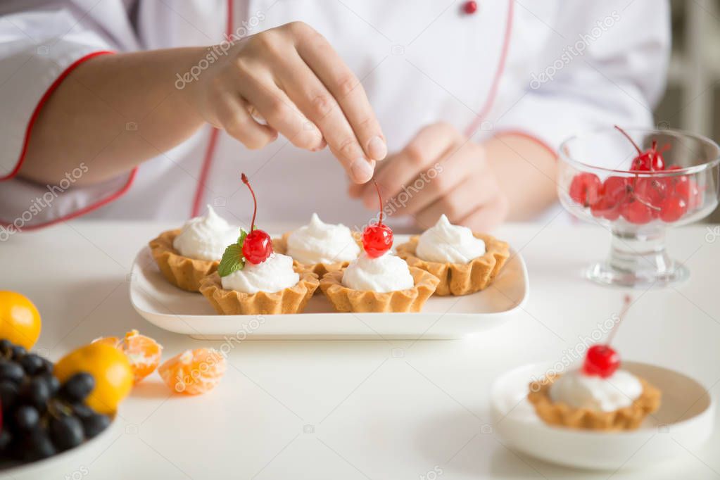 Close up of female confectioner hands topping custard tarts