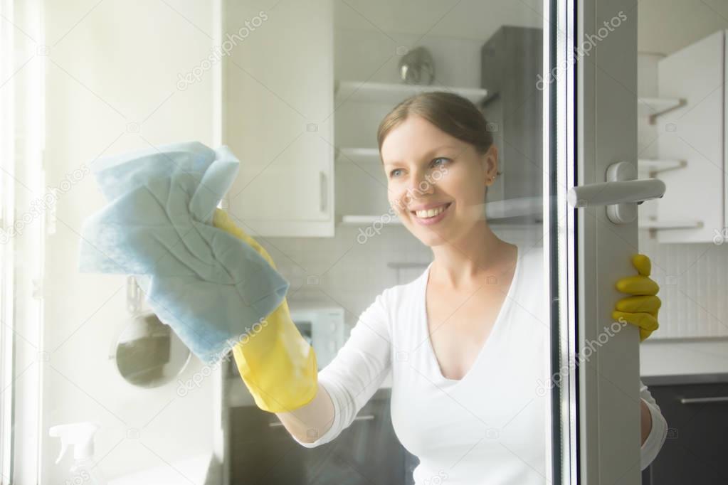 Beautiful smiling young housewife washing the windows