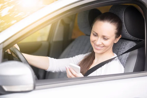 Young woman looking at her phone traveling by car — Stock Photo, Image